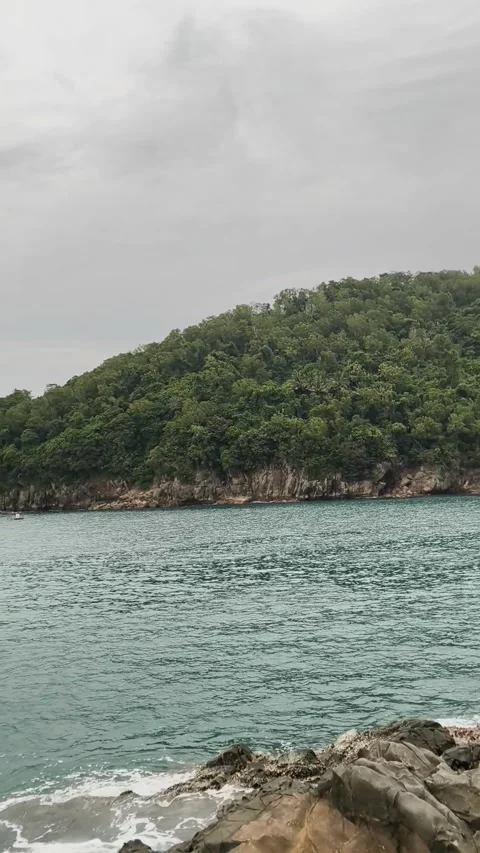 Calm Ocean Waves Crash Against Rocks with Mountains in the Backdrop 库存影片 333497981