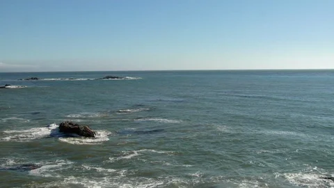 Calm ocean waves crash onto rocks and roll into shore beach Stock Footage 125341093