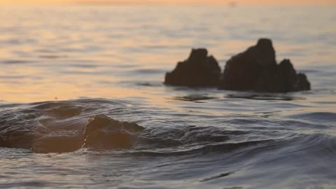 Calm ocean waves gently flowing around dark rocks during sunset. Stock Footage 337408591
