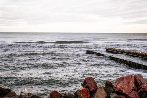 Calm Ocean Waves Gently Lap Against a Rocky Jetty at Dawn Near a Serene Coa.. Stock Photos