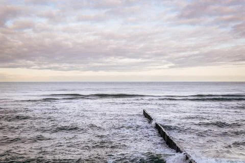 Calm Ocean Waves Gently Lap Against a Rocky Jetty at Dawn Near a Serene Coa.. Stock Photos