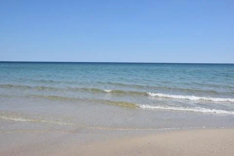 Calm ocean waves gently lapping on sandy beach under clear blue sky Фото