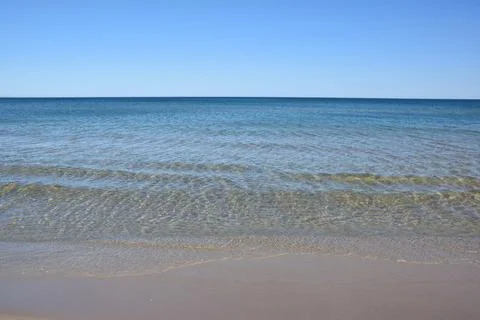 Calm ocean waves gently lapping on sandy beach under clear blue sky Stock Photos