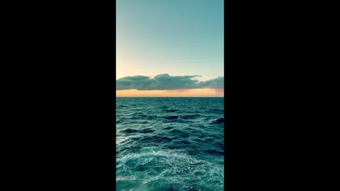 Calm ocean waves gently roll under a vibrant sunset sky with dark clouds on.. Stock Footage 338279788