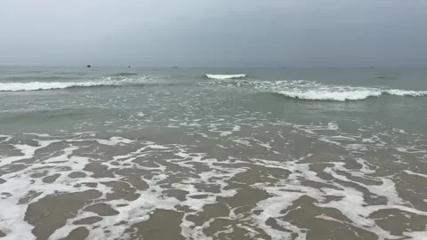 Calm ocean waves gently rolling onto a sandy beach under a cloudy sky Vidéo 334083964
