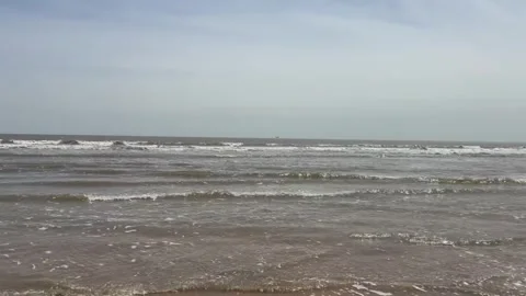Calm ocean waves gently rolling onto a sandy beach under a cloudy sky Stockbeeldmateriaal 334085047
