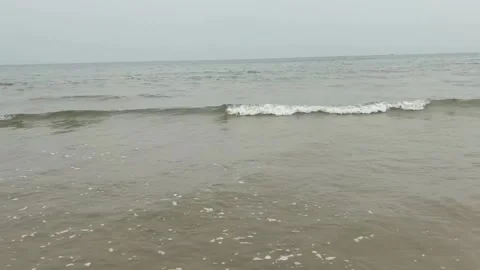Calm ocean waves gently rolling onto the sandy beach on a cloudy day Vidéo 334163222