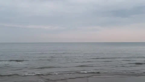 Calm ocean waves gently rolling onto a sandy beach under a soft, overcast sky at Vidéo 334163817