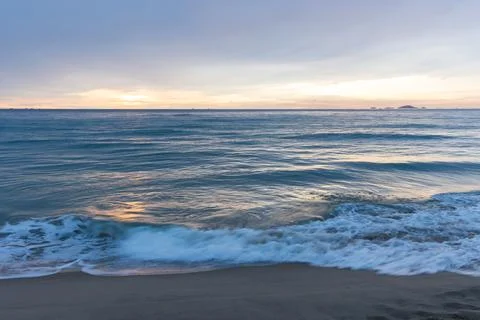 Calm ocean waves gently wash onto a sandy beach beneath a soft pastel sunri.. Stock Photos