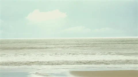 Calm ocean waves gently washing onto sandy beach under soft cloudy sky Stock Footage 285871106