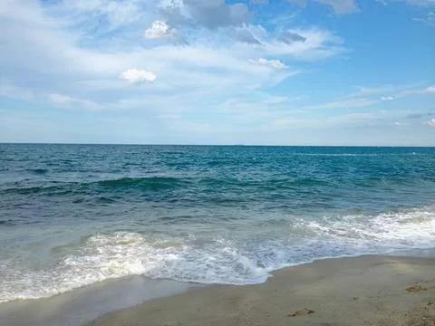 Calm ocean waves hitting sandy beach under blue sky Stock Photos