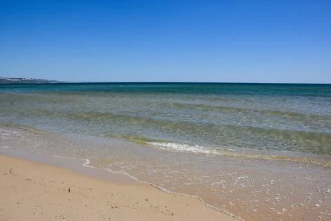 Calm ocean waves lapping on sandy beach under clear blue sky Stock Photos