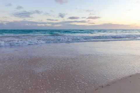 Calm ocean waves roll onto a wide sandy beach at sunset, leaving delicate foa 库存照片
