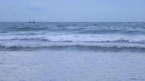Calm ocean waves rolling onto a sandy beach under a soft blue sky Video stock 347067196