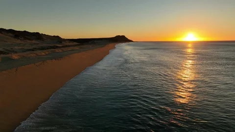 Calm ocean waves rolling up on shore as the sun rises above the horizon Stock Footage 236741973