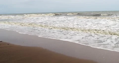 Calm ocean waves softly rolling onto sandy shore beneath blanket of clouds Stock Footage 345281715