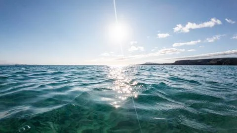 Calm ocean waves sparkling under the bright sun near a rocky coastline at midday Fotos Stock
