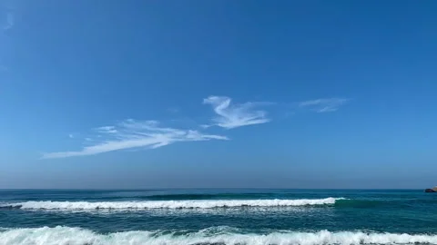 Calm ocean waves under a clear blue sky with thin clouds, slow motion Stock Footage 327583583