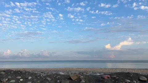 Calm pebble beach under blue sky with fluffy altocumulus clouds at sunrise Stock Footage 341754650