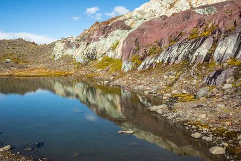 Calm pond reflecting multi-colored rock of red, purple and white. Stock Photos