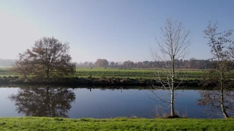 Calm river bordered by frosty grass and fenced green fields clear sky 库存影片 323359817