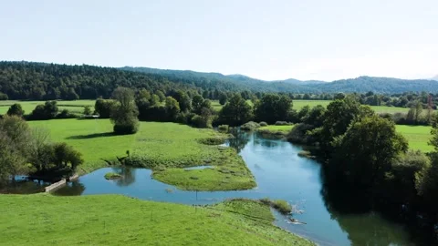 A calm river flowing through green fields and forested hills under a bright sky. Stock Footage 287114811
