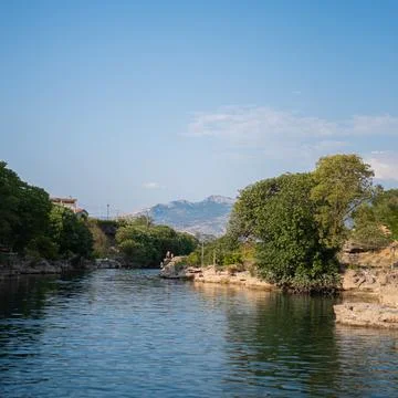 Calm river flows between rocky, tree-lined banks under a clear sky Stock Photos