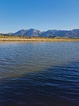 Calm river flows gently, framed by a majestic mountain range and arranged rocks Stock Photos