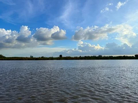Calm river flows under a partly cloudy blue sky landscape photo Foto stock