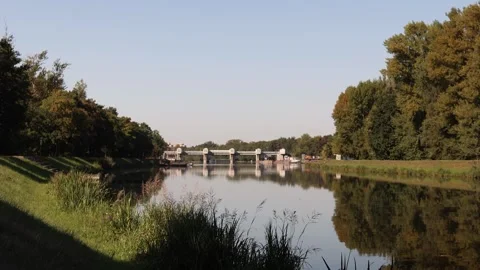Calm river with lush green trees reflecting in the water and a dam bridge struct Stock Footage 315159491