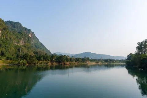 Calm river reflects distant hills and lush greenery Stock Photos