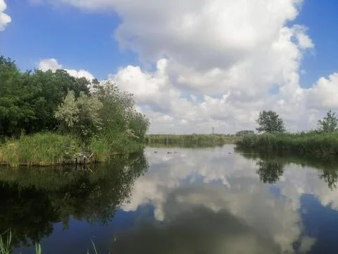 Calm river surface reflects fluffy clouds and blue sky, creating perfect vi.. Stock Photos