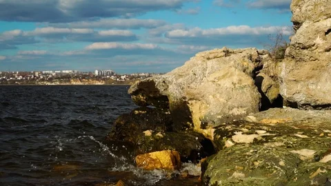 Calm river waves splash against wild nature rock beach on sunny spring day under Stock Footage 107332903