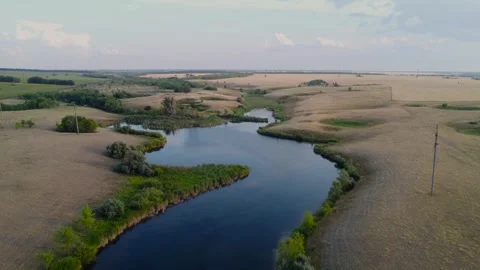 A calm river winding through lush fields in a picturesque landscape, captured by Stock Footage 282105024