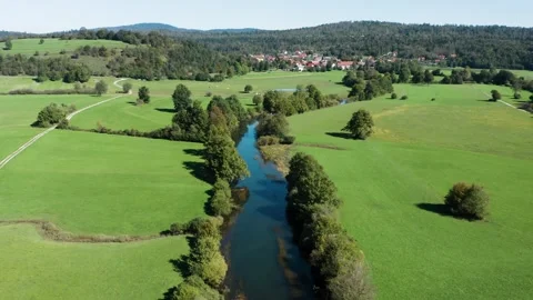 A calm river winds through green pastures and trees, reflecting the clear sky. Stock Footage 287114704