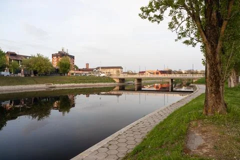 Calm Riverfront With Bridge and Reflections Along Tree-Lined Urban Walkway .. Stock Photos