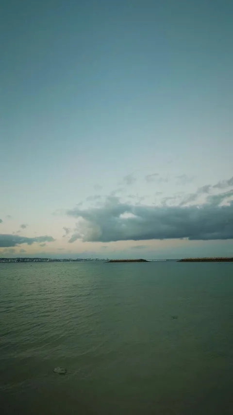 Calm sea with distant cityscape under cloudy sky at dusk Stock Footage 346269854