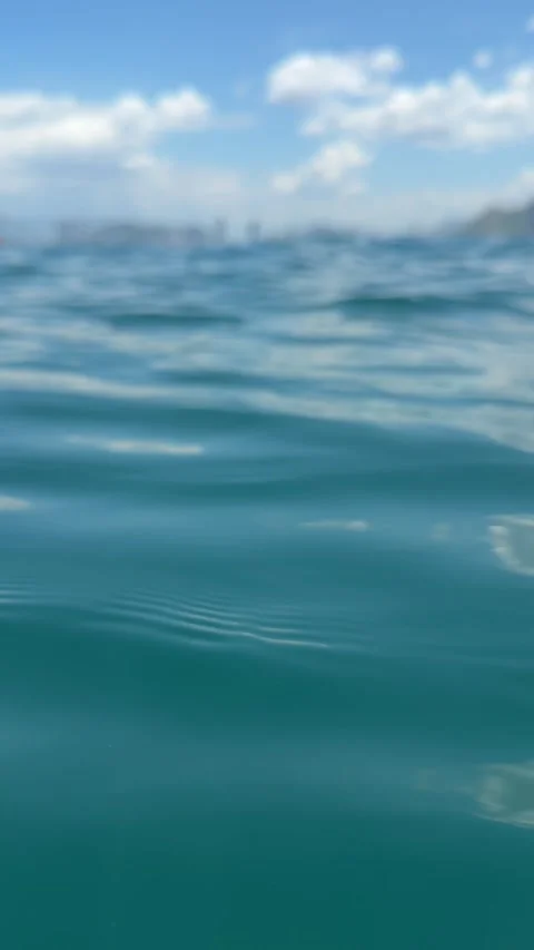 Calm sea with small waves, low horizon, and a blurred city skyline and mountains Stock Footage 340150255