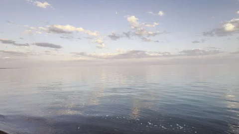 Calm Sea at Sunset with Soft Cloud Reflections and Gentle Water Ripples Stock Footage 338999401