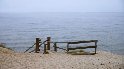 Calm sea view from sandy beach with wooden fence steps under overcast sky Stock Footage 335291063
