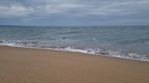 Calm sea waves gently rolling onto sandy beach under cloudy sky Stock Footage 322093016