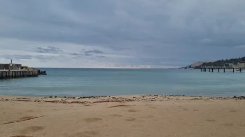 Calm sea waves by sandy beach with cloudy sky and pier Stock Footage 319985078