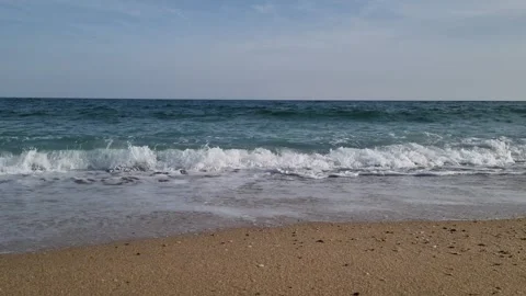 Calm shoreline with soft waves under light cloudy blue daytime sky Stock Footage 322124558