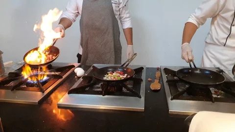 Calm skillful chefs fry delicious meals on pans using flame Stock Footage 112201341