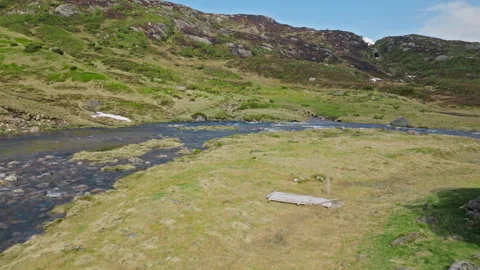 A calm stretch of mountain river curves through open grassland in Norway. Stock Footage 328131242