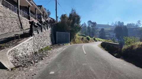 Calm, sun-drenched rural road winds uphill beside a rustic stone wall Stock Footage 345152320