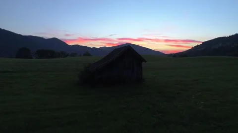 Calm sunset in the mountains with bright red sky and a cabin on the grassland Stockbeeldmateriaal 232022224