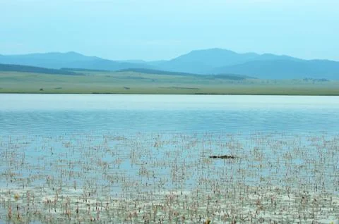 The calm surface of a large lake surrounded by blue hills painted by the sett Foto stock