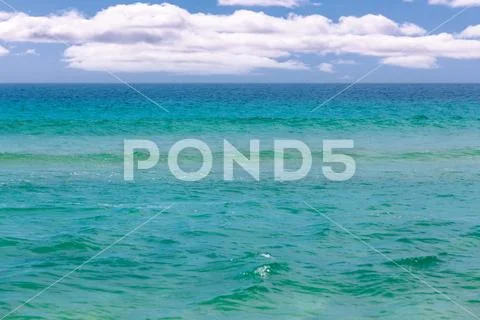 Calm turquoise ocean water under white fluffy clouds Stock Photos