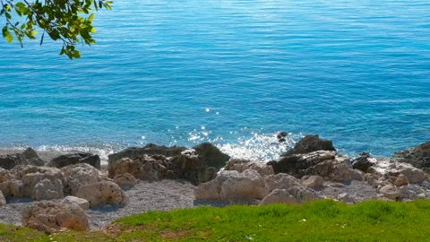 Calm turquoise sea gently lapping rocky coastline on sunny day Stock Footage 321027256